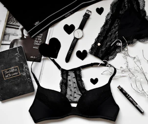 A stylish black cap and a sensual lingerie set laid out on a soft bedspread.