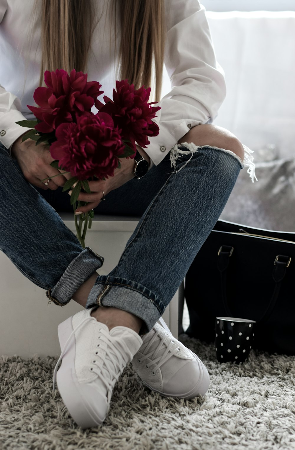 femme tenant des fleurs rouges assise sur une surface blanche