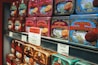 Rows of colorful vintage-style tin boxes are displayed on shelves, each containing La Mere Poulard butter cookies. The packaging features intricate designs and illustrations, emphasizing a traditional and artisanal product. Prominent signage with pricing and promotional offers is visible, indicating a special sale.