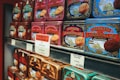 Rows of colorful vintage-style tin boxes are displayed on shelves, each containing La Mere Poulard butter cookies. The packaging features intricate designs and illustrations, emphasizing a traditional and artisanal product. Prominent signage with pricing and promotional offers is visible, indicating a special sale.