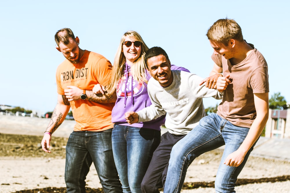 four smiling people linking arms during daytime