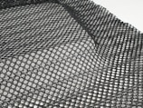 A detailed black mesh material with intricate patterns is laid out, displaying a grid of interlocking loops and open spaces. The texture appears flexible and lightweight, with subtle shadows adding depth.