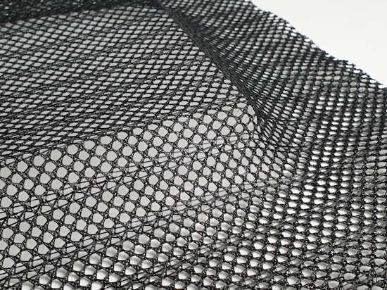 A detailed black mesh material with intricate patterns is laid out, displaying a grid of interlocking loops and open spaces. The texture appears flexible and lightweight, with subtle shadows adding depth.