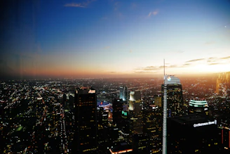 A high-angle shot of a bustling city skyline at sunset with glowing lights.