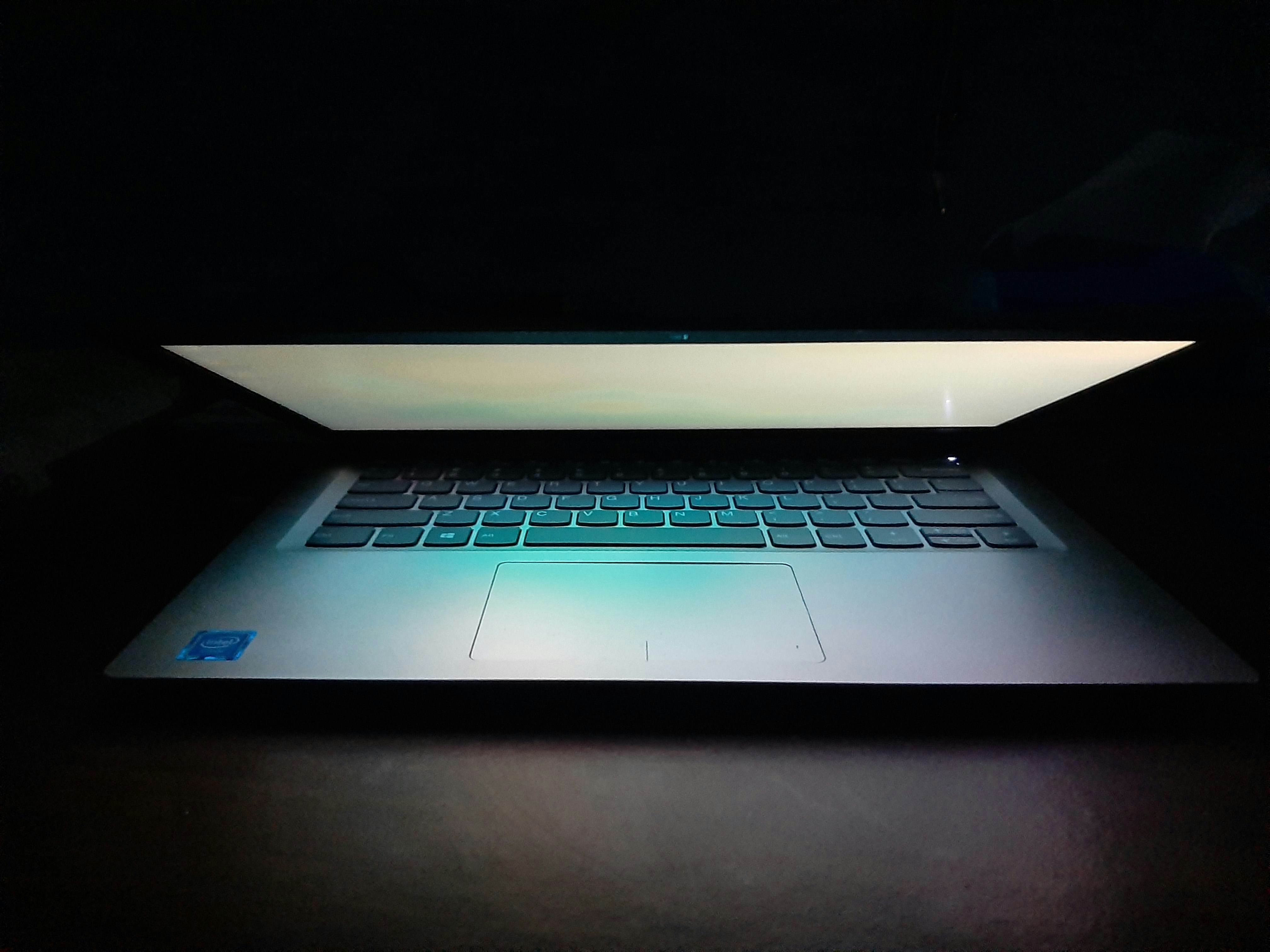 Thin silver laptop open showing vibrant display in dark studio setting