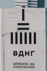 A sign with black geometric shapes resembling bars and a vertical line. The background is white and displays Cyrillic text below the symbols, suggesting a message related to parking payment.