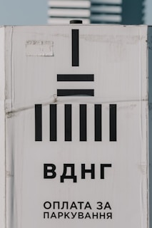 A sign with black geometric shapes resembling bars and a vertical line. The background is white and displays Cyrillic text below the symbols, suggesting a message related to parking payment.