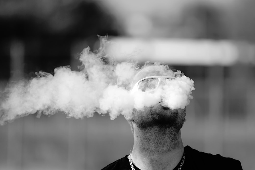 time lapse grayscale photography of man blowing smoke from his mouth