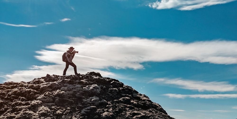 man wearing gray dress shirt and gray pants standing on mountain taking photo