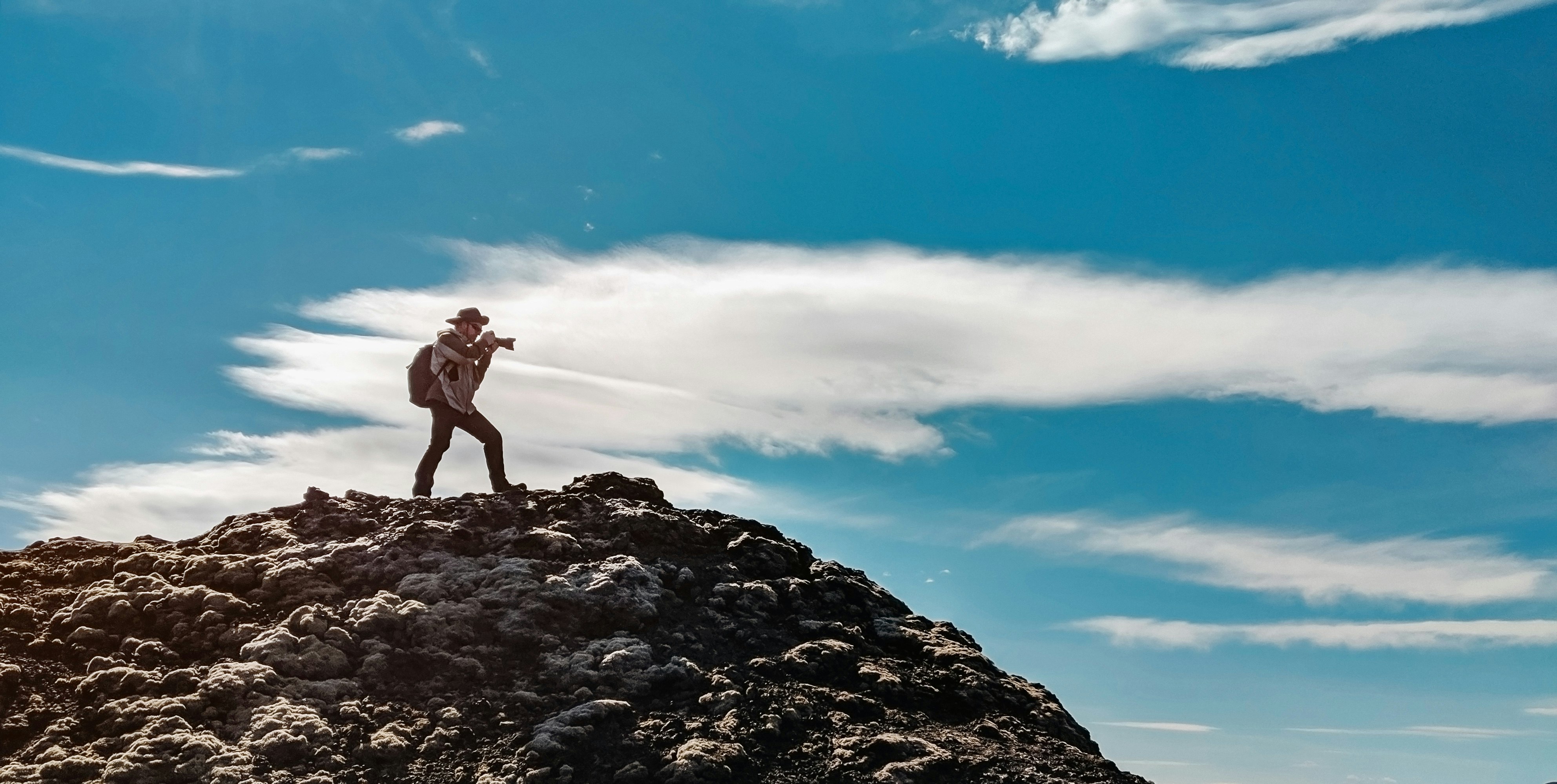 man wearing gray dress shirt and gray pants standing on mountain taking photo