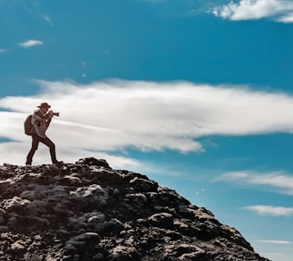 man wearing gray dress shirt and gray pants standing on mountain taking photo