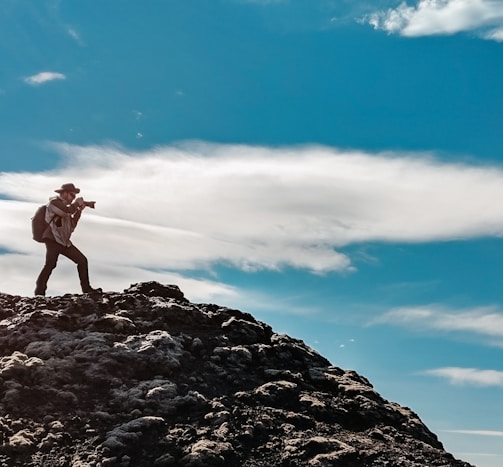 man wearing gray dress shirt and gray pants standing on mountain taking photo