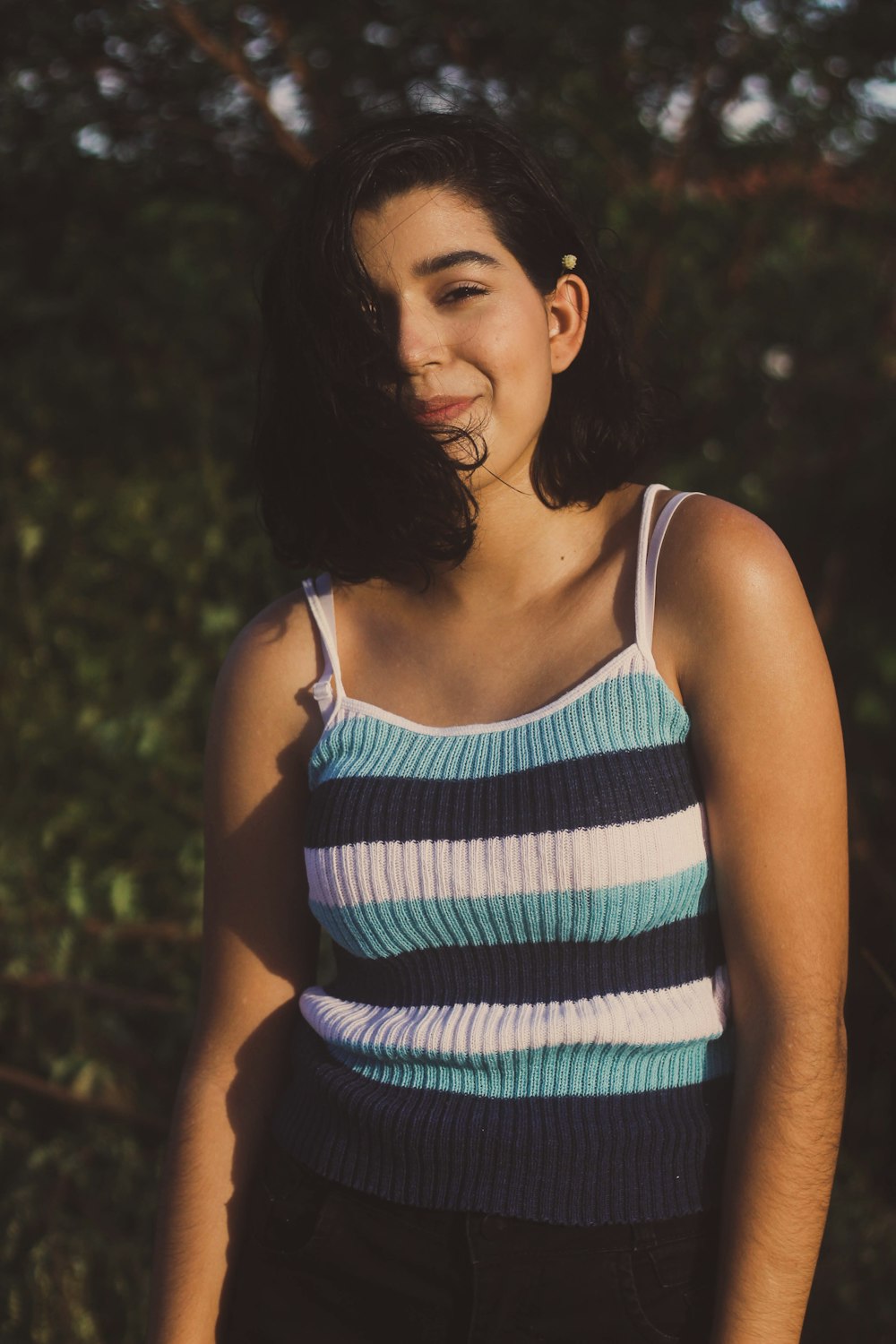 woman in teal, white, and black spaghetti strap top standing outdoors