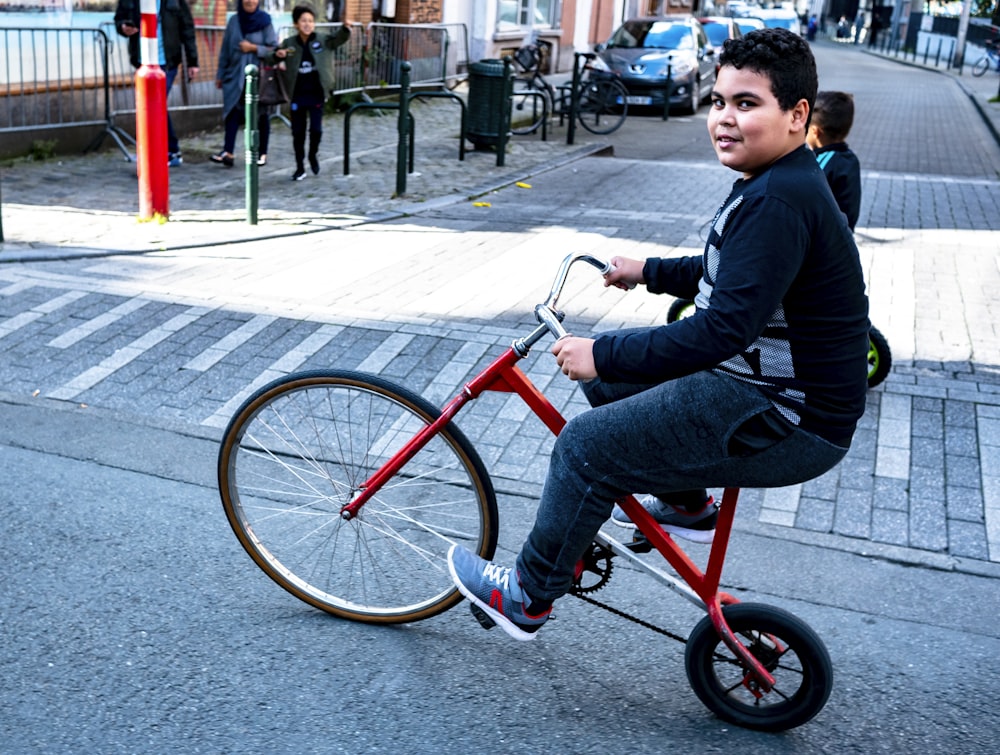 man wearing black and gray long-sleeved shirt and gray track pants riding red bike