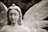 A serene stone statue of an angel with gentle features and detailed, feathered wings. The angel has a calm expression with closed eyes and wavy hair. A small star adorns its head, giving it an ethereal quality.