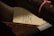 A close-up view of a parcel or packaging with a label containing text in Hebrew and English. The label reads 'JERUSALEM P.P. 9258' and is attached to what looks like a rolled-up item secured with a string. The background shows various shades of brown materials, suggesting a rustic or vintage setting.