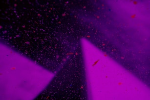 A cosmic scene with a deep purple background speckled with variously sized dots resembling stars or particles. Bright triangular shapes in a lighter purple hue intersect the image, adding depth and contrast.
