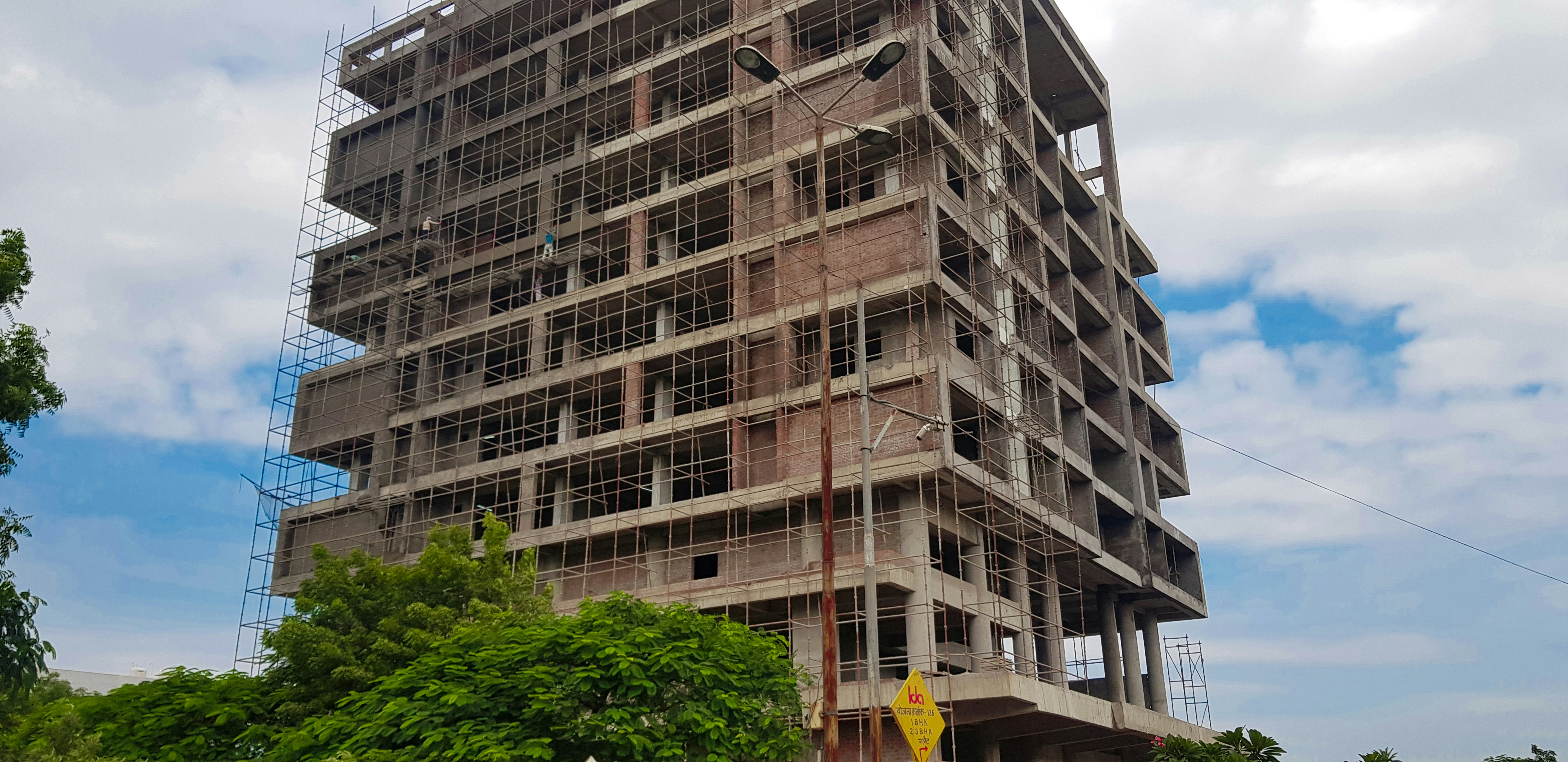Multi-storey commercial building under construction, scaffolding and concrete framework, overcast sky, dark shadows
