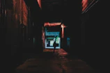 A shadowy alley bathed in deep red neon light, with a lone figure cloaked in mystery.