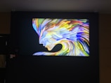 A vivid and colorful abstract painting of a human face profile, composed of dynamic, swirling brushstrokes. The face appears to be flowing, merging with the background in a spectrum of bright colors such as blue, yellow, orange, and green, giving a sense of movement and energy.