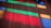 Colorful beams of light in red, green, and blue cast onto a wooden floor, creating a vibrant pattern. A circular white object and part of a black item are visible on the floor.