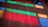 Colorful beams of light in red, green, and blue cast onto a wooden floor, creating a vibrant pattern. A circular white object and part of a black item are visible on the floor.