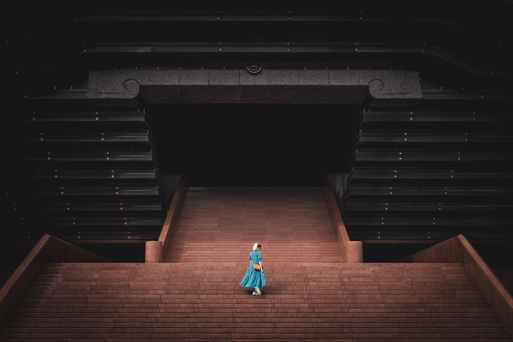 a woman in a blue dress walking up a set of stairs