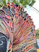 An intricate and colorful carnival costume with layered, circular patterns that resemble a peacock's feathers. The design is made up of beads and fabrics in a wide range of colors, forming a vibrant and dynamic arrangement.