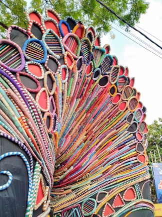 An intricate and colorful carnival costume with layered, circular patterns that resemble a peacock's feathers. The design is made up of beads and fabrics in a wide range of colors, forming a vibrant and dynamic arrangement.