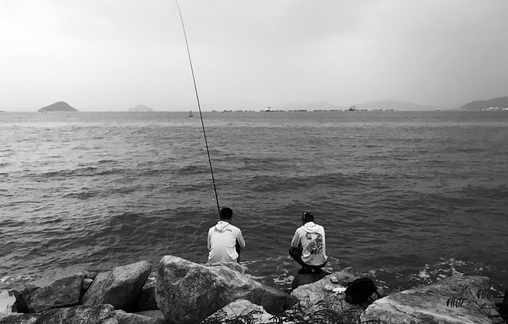 grayscale photography of two person fishing viewing mountain