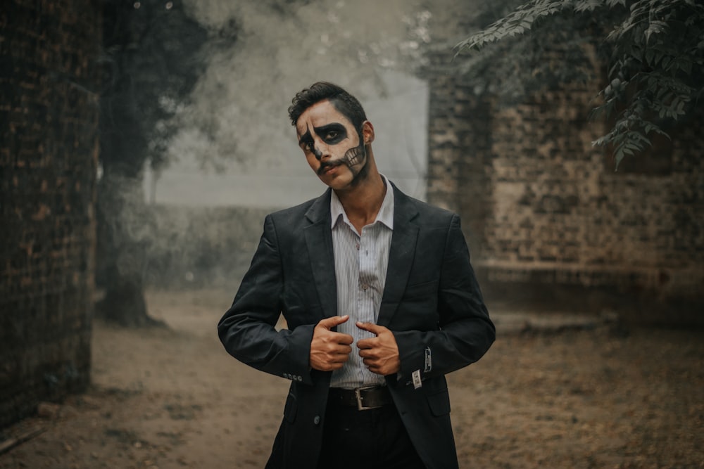 man wearing black notched lapel suit jacket with Halloween art on face standing