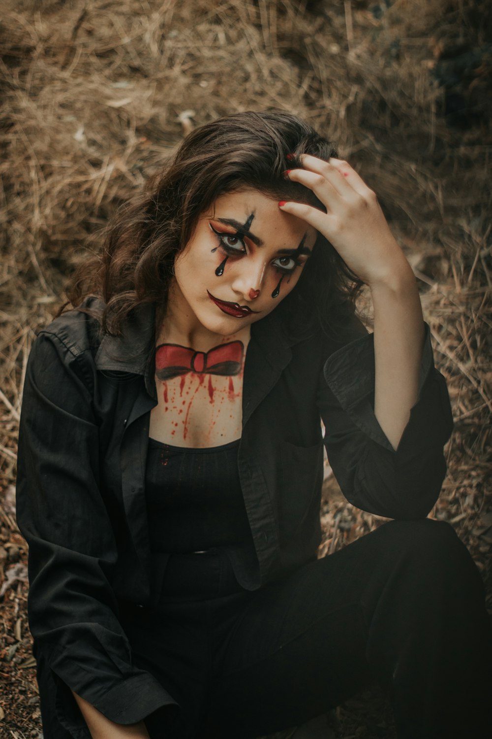 woman wearing black collared button-up long-sleeved shirt with Joker paint on face sitting while touching her head