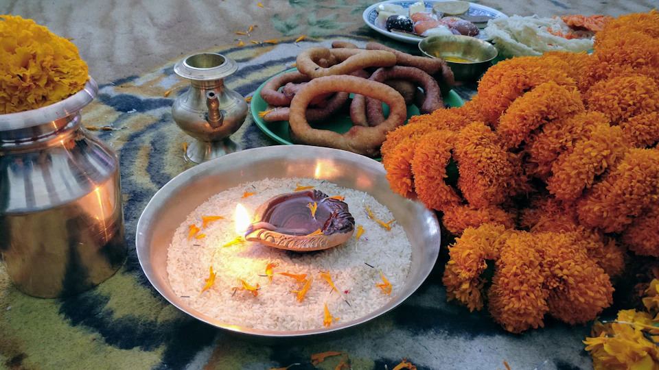 Rings of fried sel roti on a plate beside a lit clay lamp and marigolds laid out for Tihar