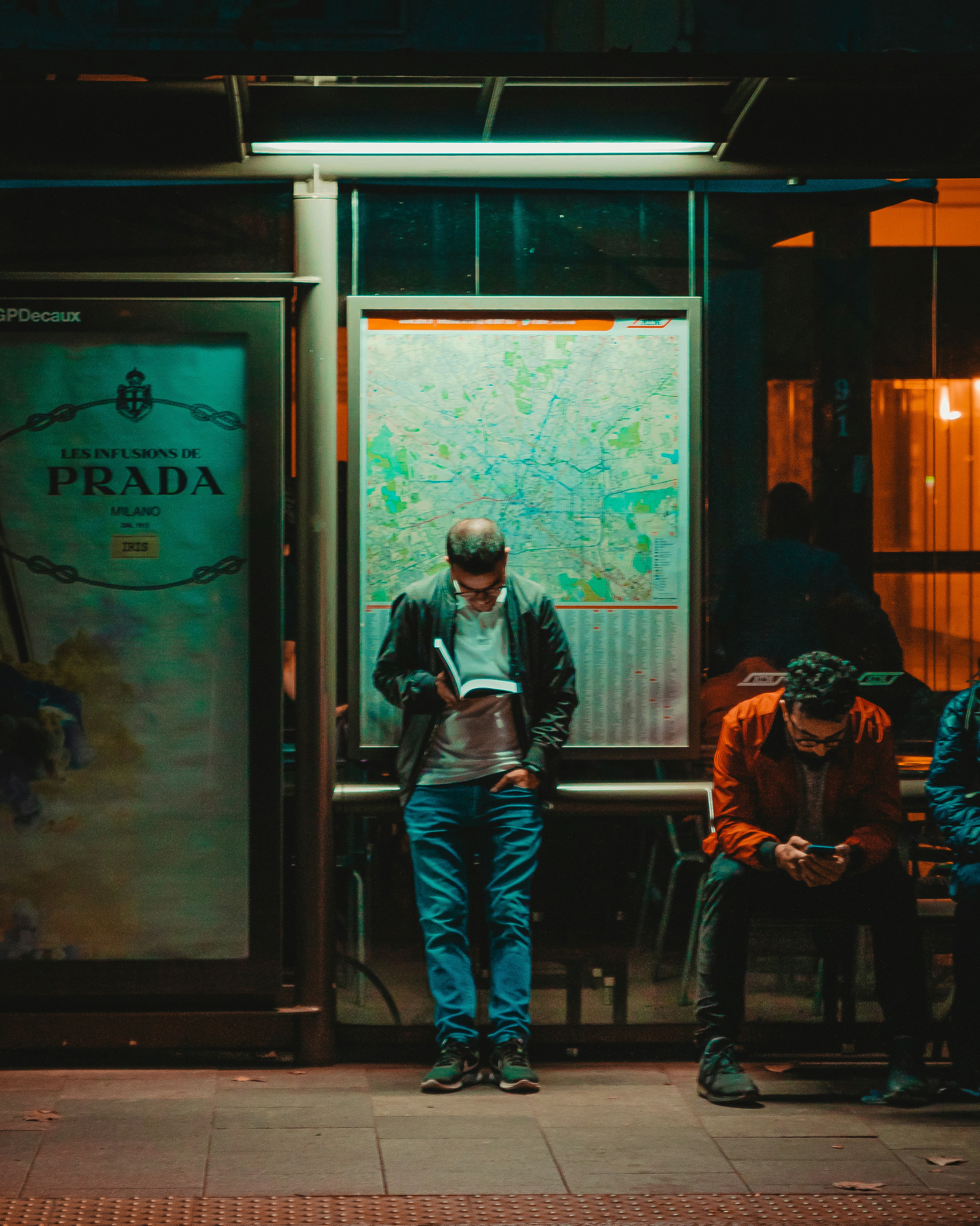 standing man reading book beside sitting man using phone