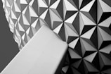 A geometric pattern composed of repeating triangular shapes creates a visually striking design. The structure features a combination of light and dark shades, giving it a modern, abstract appearance. The smooth, angular surface adds a sense of depth and intrigue.