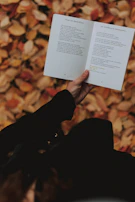 A smiling reader holding 'Spark of Valor' with a backdrop of autumn leaves.