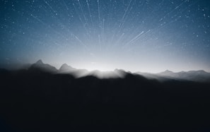 Nighttime view of a mountain range silhouetted against a starry sky with shimmering silver highlights.