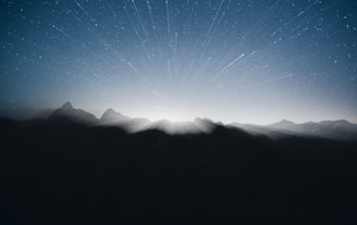 Nighttime view of a mountain range silhouetted against a starry sky with shimmering silver highlights.