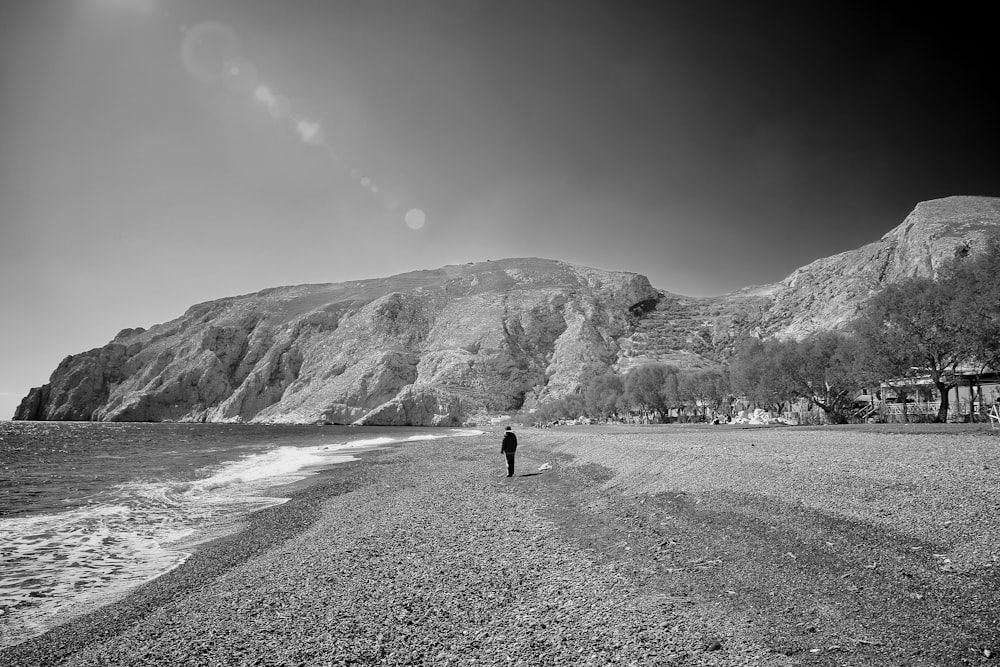 greyscale photo of person walking on seashore