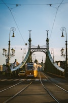 Historic trams crossing Liberty Bridge on a bright, clear day.