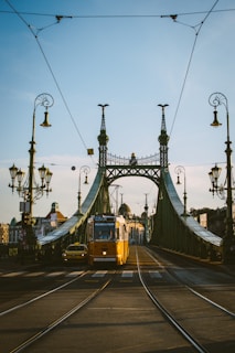 Historic trams crossing Liberty Bridge on a bright, clear day.