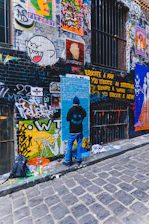 Urban alleyway covered in bold, colorful street art with workshop attendees painting.