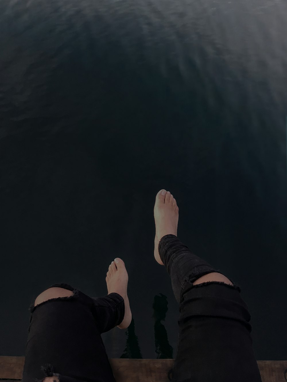 person sitting on brown wooden plank in front of calm body of water