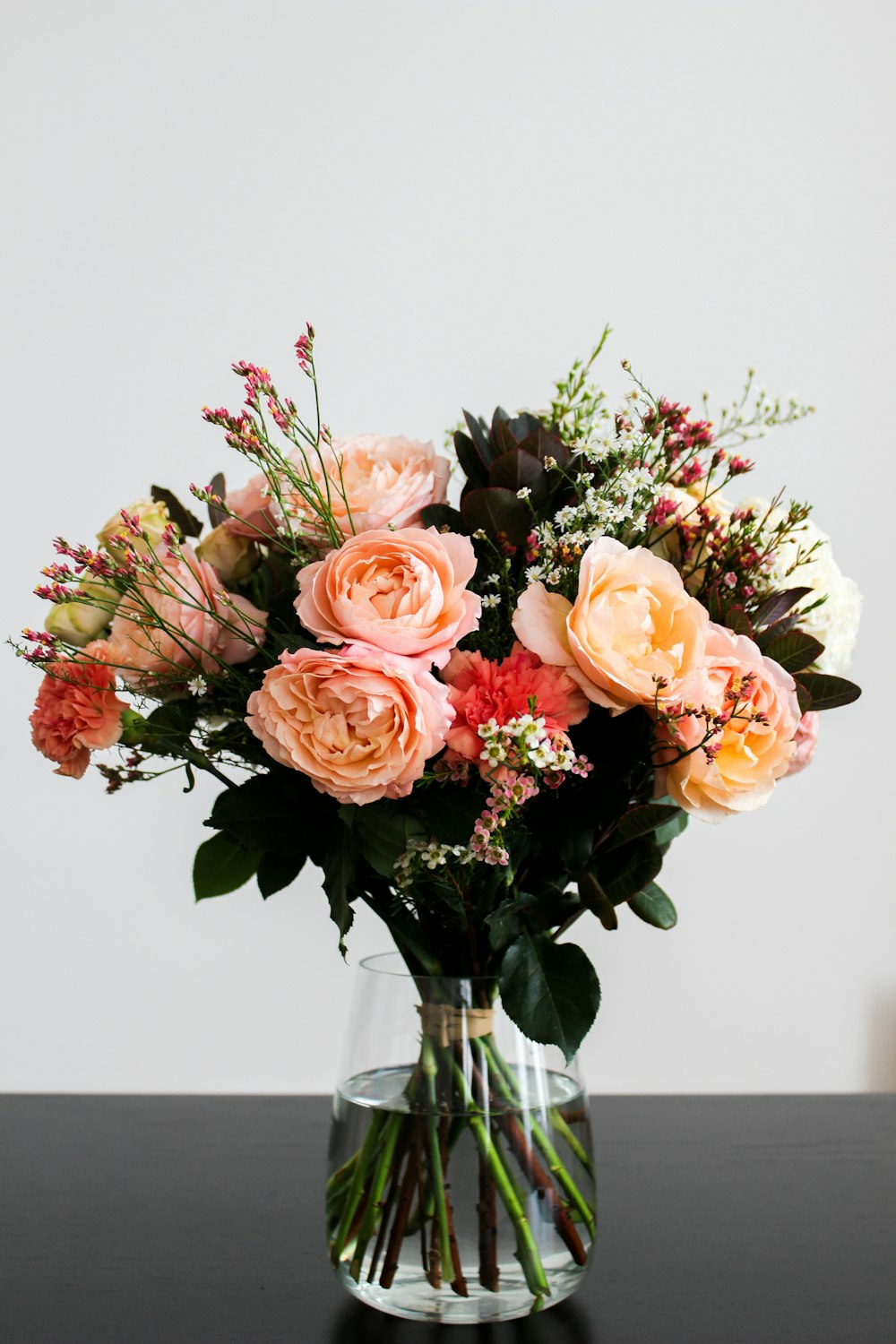 Bouquet de fleurs roses, beiges et rouges dans un vase en verre transparent