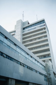 A multi-story, modernist-style building with a series of vertical and horizontal lines formed by windows and concrete panels. Antennas are mounted on the rooftop, and the facade is mostly composed of gray concrete and glass, reflecting a clear sky.