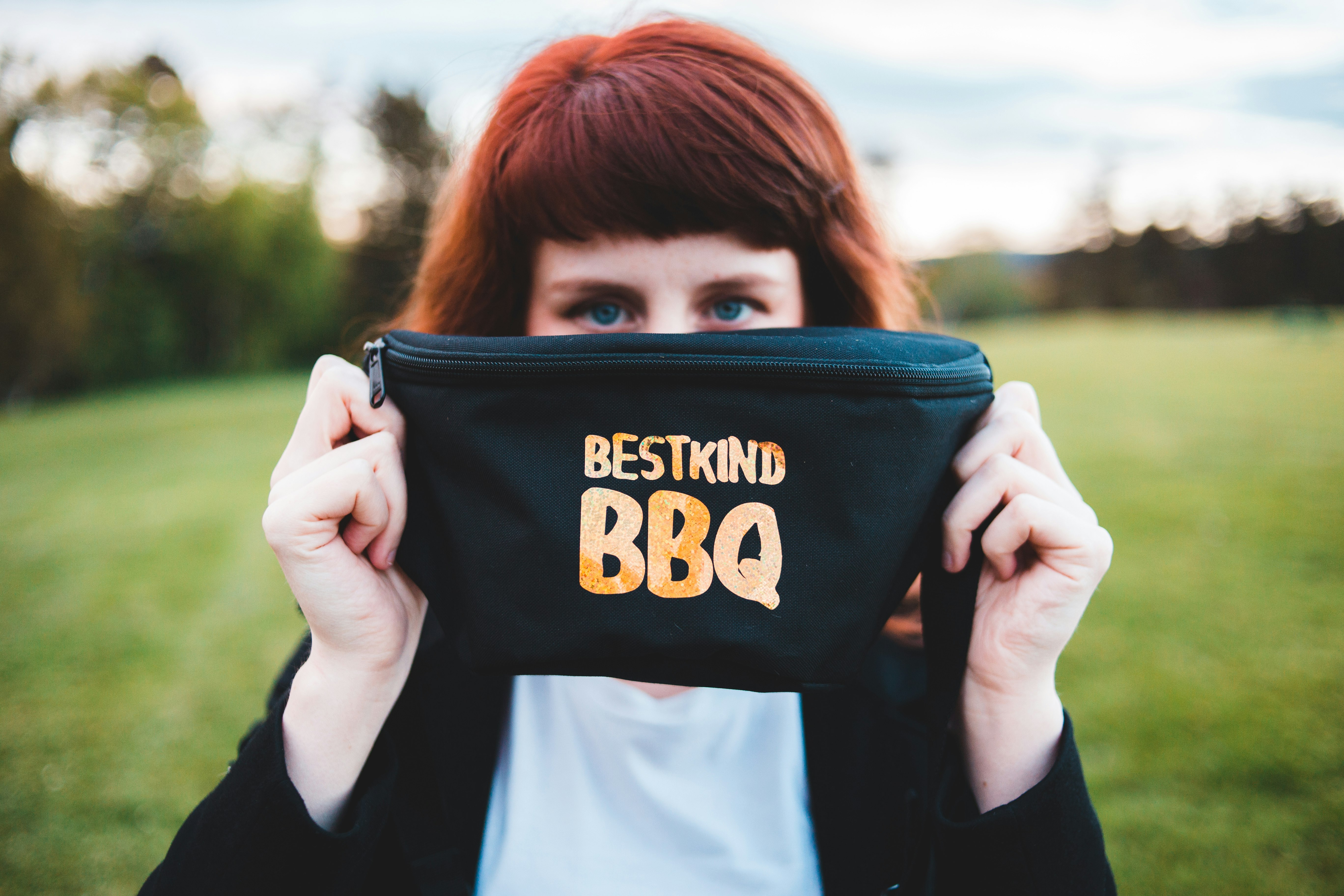 woman covering face using black and yellow Best Kind BBQ fanny pack