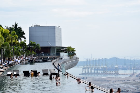 people in swimming pool viewing buildings and mountain under white and blue sky during daytime in Sands SkyPark Observation Deck Singapore