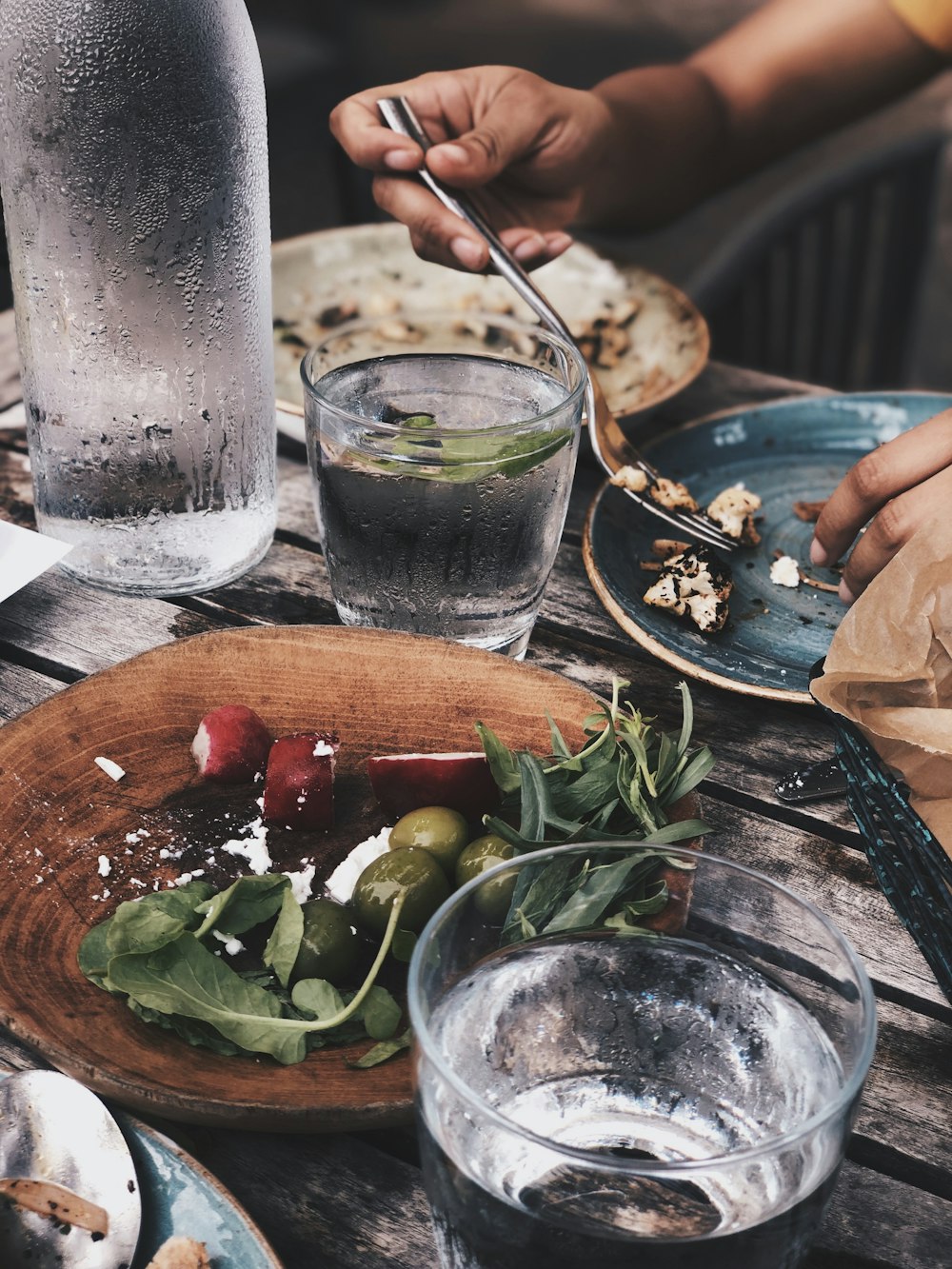 person using gray stainless steel fork and water in drinking glass on table