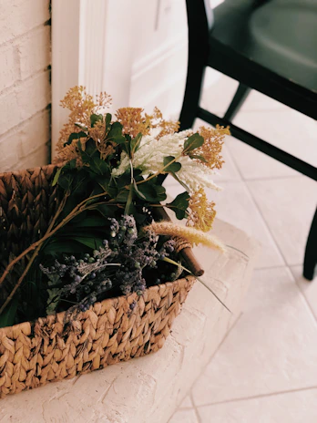Close-up of a decorative basket filled with fresh flowers beside a rustic bench stool.