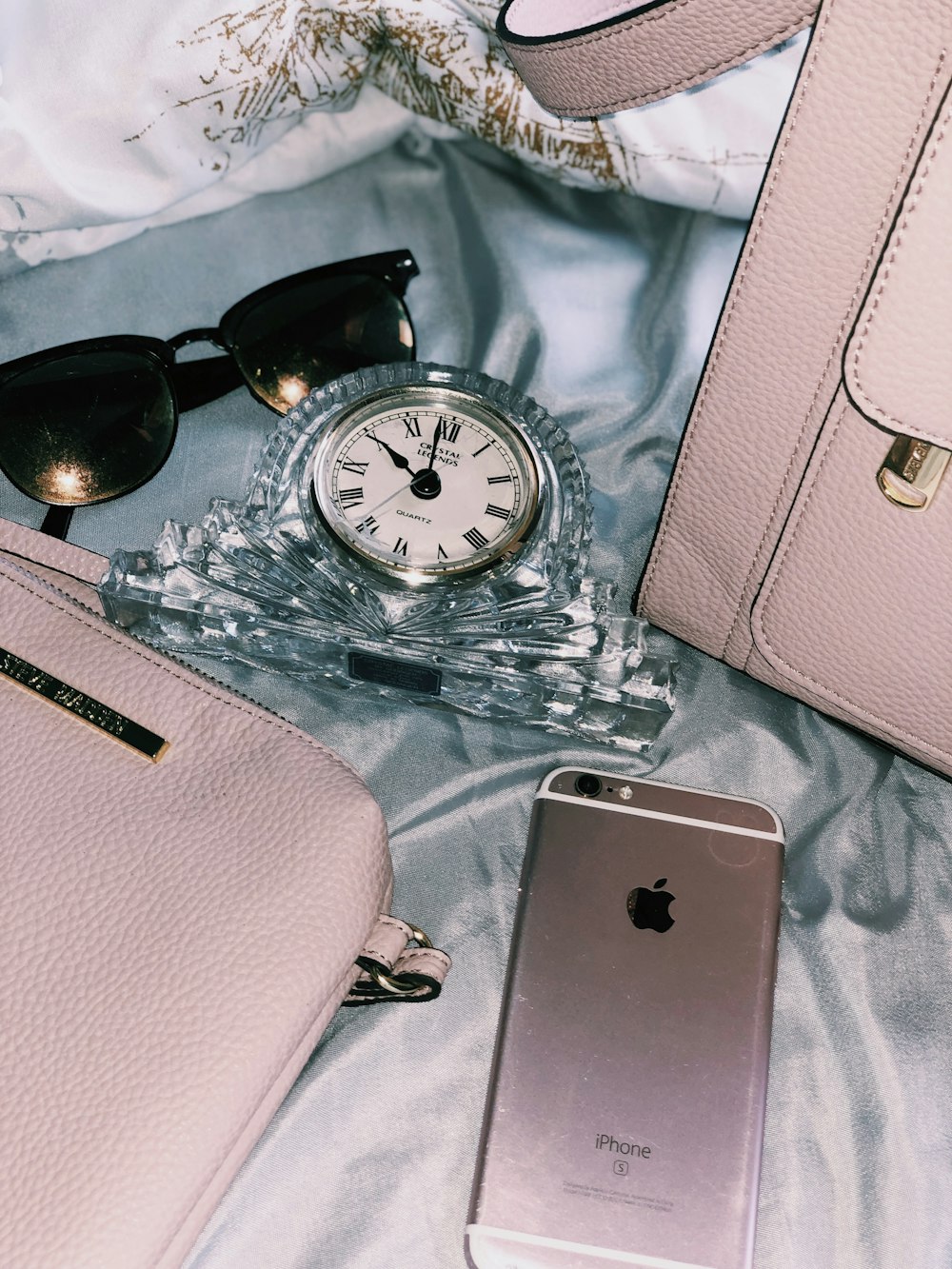 gold iPhone 6s near black framed sunglasses, pink leather bag, and clear analog clock